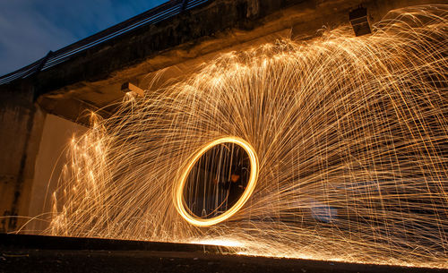 Blurred motion of man standing by illuminated lights against sky at night