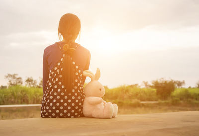 Rear view of woman sitting toy against sky during sunset