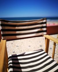 Close-up of chairs on table at beach against clear blue sky