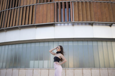 Full body low angle side view of young woman wearing elegant clothes standing on city street