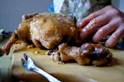 Cropped image of hand cutting roasted duck on board