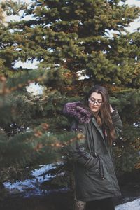 Portrait of smiling young woman standing by tree during winter