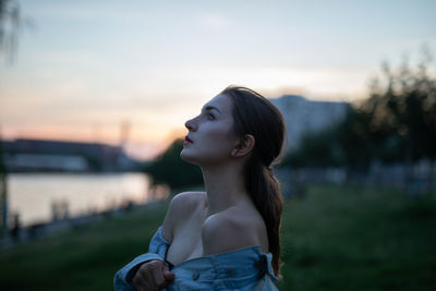 Woman looking away while standing against sky during sunset