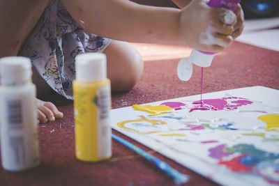 Cropped image of girl pouring watercolor paints on paper at home