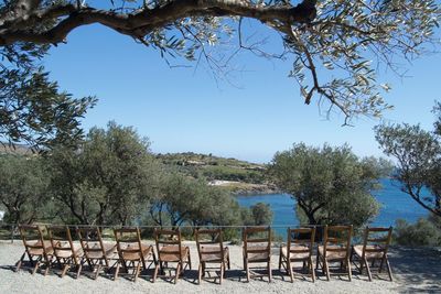 Empty chairs and table by trees against clear blue sky