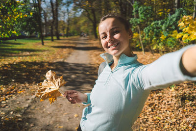 Beautiful girl taking picture of herself while walking in a sunny autumn forest