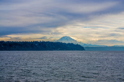 Scenic view of sea by snowcapped mountains against sky during sunset