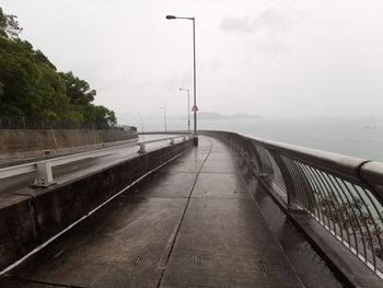 Empty road by railing against sky