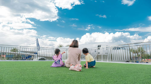 The back view of happy family mother woman and baby kids, pointing fun to the plane.