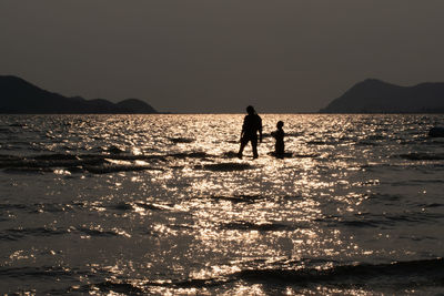 Silhouette people on sea by mountains against clear sky