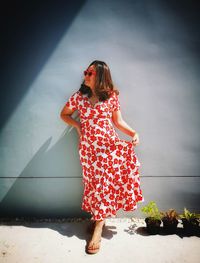 Midsection of woman standing against wall and wearing red flower dress.