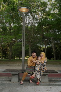 Couple sitting on sidewalk against trees