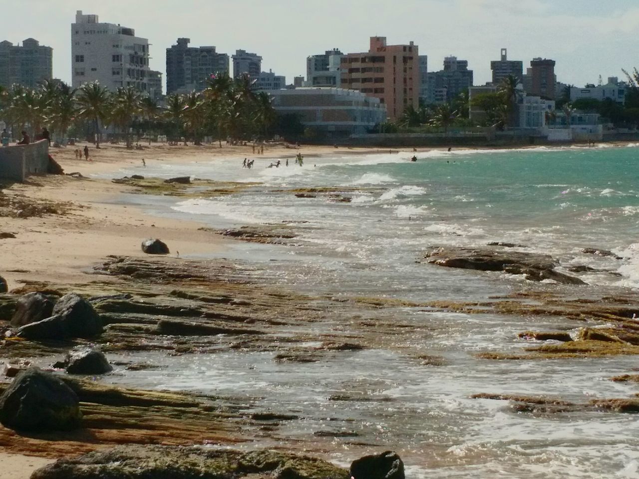 building exterior, water, architecture, built structure, city, sea, beach, shore, rock - object, cityscape, wave, surf, coastline, incidental people, sky, residential building, sand, bird, city life, river