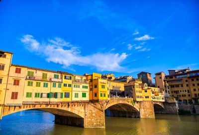 Arch bridge over river against blue sky in city