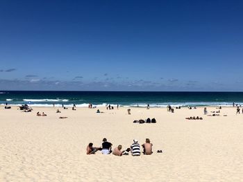 Group of people at beach against clear blue sky