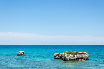 Rocks by sea against blue sky