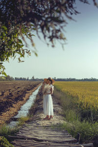 Full length portrait of woman standing on field against sky