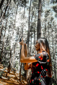 Young woman holding tree trunk in forest