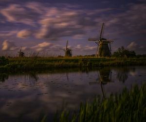 Traditional windmill by lake against sky during sunset