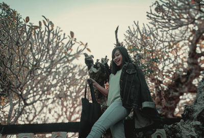 Low angle view of woman standing by plants against sky during winter