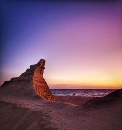 Rock formation on beach against sky during sunset