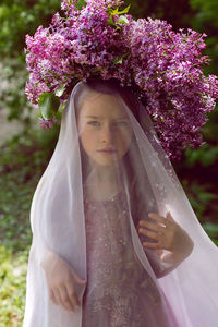 Caucasian girl child seven years old in a purple dress stands in nature with a wreath of lilacs