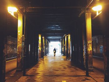 Rear view of person walking on illuminated footpath under bridge
