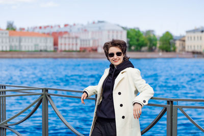 Beautiful young woman walks along embankment in white coat and black sweatshirt