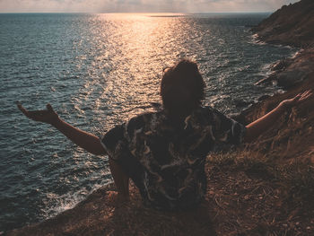 Rear view of man standing by sea against sky during sunset