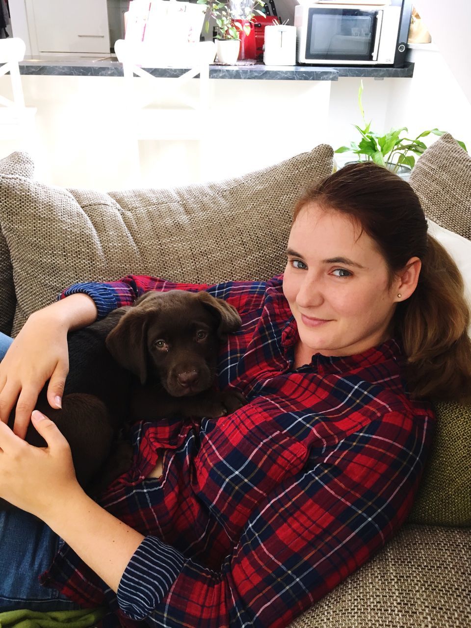 looking at camera, sofa, dog, portrait, one animal, pets, home interior, indoors, real people, mammal, casual clothing, animal themes, lifestyles, relaxation, smiling, domestic animals, living room, one person, comfortable, sitting, young adult, young women, day, friendship, home showcase interior