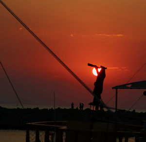 Silhouette man fishing in sea against orange sky
