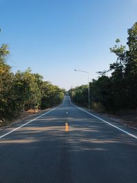 Empty road amidst trees against clear sky