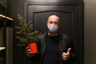 A bald man in protective mask stands in doorway with small artificial christmas
