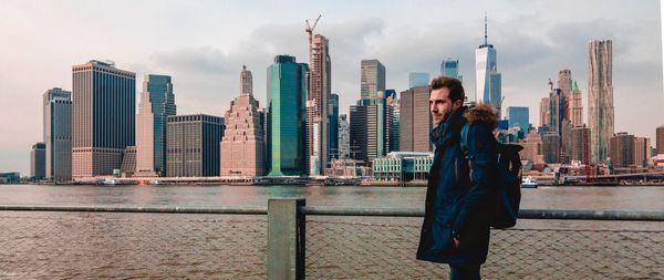 Man standing by modern buildings in city against sky