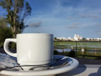 Close-up of cup in plate on table against sky