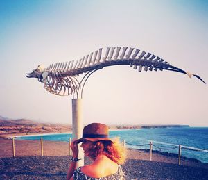 Woman standing by animal skeleton at beach against sky