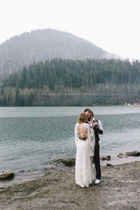 Happy newlyweds in love a man and a woman in wedding clothes embrace on the shore of the lake