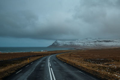 Empty road leading towards snowcapped mountain against sky