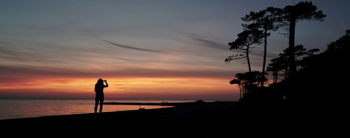 Silhouette woman standing on beach against sky during sunset