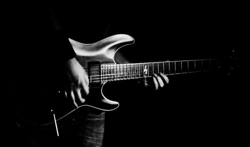 Midsection of man playing guitar against black background