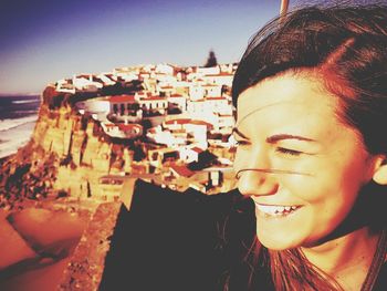 Close-up of smiling young woman in city against sky