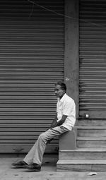 Side view of young man sitting against closed shutter