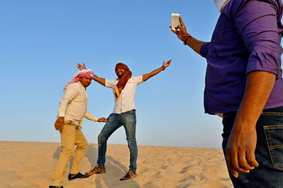 Midsection of man photographing friends while standing on sand