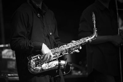 Midsection of man playing saxophone in darkroom