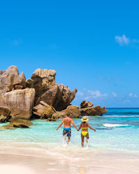 Rear view of woman standing at beach against blue sky