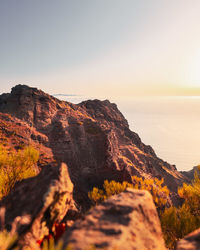 Rock formations by sea against clear sky during sunset