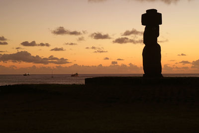 Silhouette statue on beach against sky during sunset