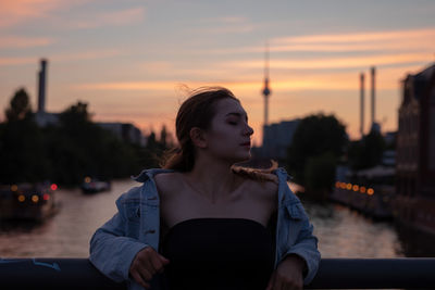 Young woman standing by railing against sky during sunset