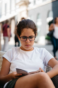 Young woman reading menu while sitting on chair at sidewalk cafe