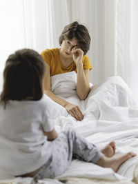 Kid wakes his mother up. sleepy disheveled mom sits in bed. uneasy life as parent. 